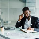 young-african-businessman-working-office-laptop-make-notice-notebook