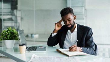 young-african-businessman-working-office-laptop-make-notice-notebook
