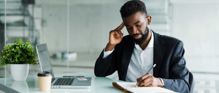young-african-businessman-working-office-laptop-make-notice-notebook